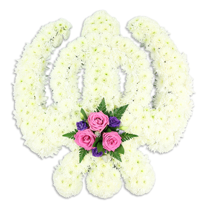 A beautifully crafted Sikh Khanda floral tribute fills the frame, set crisply against a clean white background that accentuates every contour of the sacred symbol. The Khanda's distinctive form - a central upright double-edged sword, encircled by a flawless ring, with two curved kirpans crossing at the base - is completely coated in small, tight white chrysanthemum blooms. Each flower head is carefully aligned to follow the lines of the emblem, so the edges are clearly defined yet softened by petals, like fine embroidery worked in living blossoms. The surface appears plush and even, with a gentle play of light and shadow across the layered petals, giving depth to the pure white design. At the point where the lower blades meet, a vivid accent arrangement is cradled within the floral outline. Three rich pink roses sit prominently at the centre, their petals plump and velvety, suggesting they have just been placed by caring hands. Nestled around them are several deep purple flowers - perhaps freesias or lisianthus - their slender petals adding a note of solemn richness. Sprays of dark green fern and leafy foliage weave between the blooms, framing the colours and enhancing the sense of natural abundance. A soft shadow beneath the tribute lifts it subtly from the background, making it appear almost sculptural. This is the kind of bespoke piece that might be ordered from a trusted local florist in Willesden to accompany a Sikh funeral cortege or to stand near the front of a service, offering a serene, floral expression of faith, honour, and everlasting remembrance.