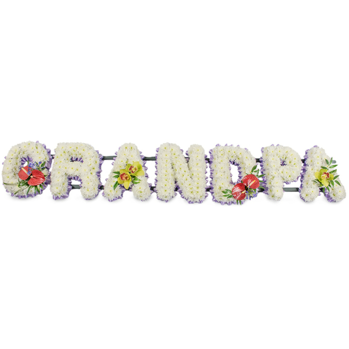 This image shows a striking funeral flower tribute arranged to spell GRANDPA in bold, block capitals, laid out in a long row as you might see it resting by a graveside in Willesden Cemetery. The letters are formed from tightly clustered white chrysanthemums, each small bloom perfectly fresh, their petals overlapping to create a dense, cushiony surface. The white is bright yet soothing, suggesting purity, peace, and the quiet gratitude that often surrounds the memory of a much-loved grandparent. Along the lower edge of each letter runs a border of soft lavender ribbon, providing a gentle lilac shadow that defines the shape of the word and adds a delicate, respectful finish.
The letters are mounted on dark green framework bars, which lend structure and a subtle line of colour beneath the blossoms. Throughout the word, the florist has woven in vivid accent sprays. The 'G' displays a bold cluster of deep red anthuriums, their waxy, heart-shaped blooms and golden spadices emerging from a bed of rich green foliage and hints of tiny purple fillers. This same combination appears again on the 'D', drawing a visual connection across the tribute and echoing the depth of feeling held for the grandfather. The first 'A' and final 'A' are softened with elegant yellow-green orchids, their intricate petals and spotted centres nestled among glossy leaves, lending a more delicate, refined beauty.
The composition feels thoughtfully balanced, as if created by an experienced local florist who understands the quiet streets around Willesden Green and the need for flowers that speak gently when words are hard to find. It is a bespoke memorial arrangement, ideal for a funeral, wake, or memorial service, offering a dignified tribute to a cherished grandfather's life.
