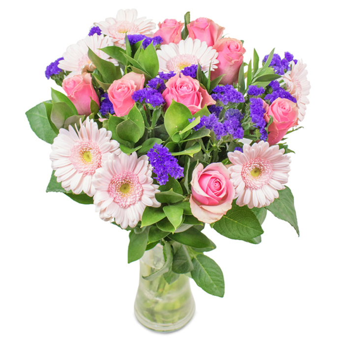 Elegantly set against a pristine white background, this vibrant bouquet from Flowers Willesden brings together the gentle romance of soft to medium pink roses-each bloom caught in its perfect moment, petals either just opening or still wrapped in a classic spiral-with the cheerful, pale pink heads of gerbera daisies, their ring of slender petals radiating outward around creamy centers. Clusters of lively purple statice are woven throughout, adding both texture and a deep pop of colour suggestive of wild blossoms picked from the edges of Willesden's many green spaces. The fresh, abundant green foliage spreads beneath, enhancing the bouquet's overall vitality and giving a sense of lushness and longevity, as if it has just arrived from the Willesden Green flower market. All stems are artfully displayed in a tall, transparent glass vase with visible water and vivid stalks extending down, amplifying the sense of brightness and clarity. This uniquely blended arrangement-pink roses and gerbera daisies accented by purple statice-radiates feelings of celebration and affection. Suitable for birthdays, anniversaries, Mother's Day, or simply as a statement piece for a home or office in Willesden, it is crafted with a keen eye for harmony and designed to delight any recipient with its local charm and freshness.